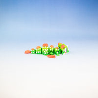 A small green caterpillar-like toy with orange flowers and white spots, lying on a white surface against a blue gradient background.