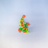 A small decorative Christmas tree-shaped ornament or figurine made from layered green, white, and orange materials, centered on a plain light gray background.